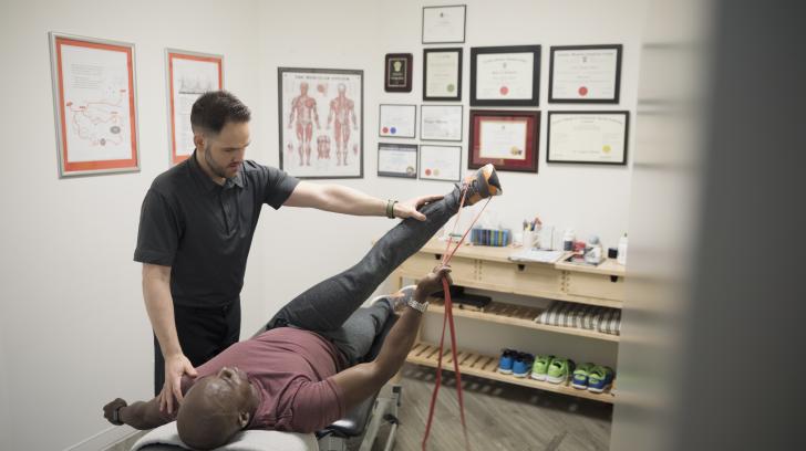 African American male patient in physical therapy using stretch band on leg