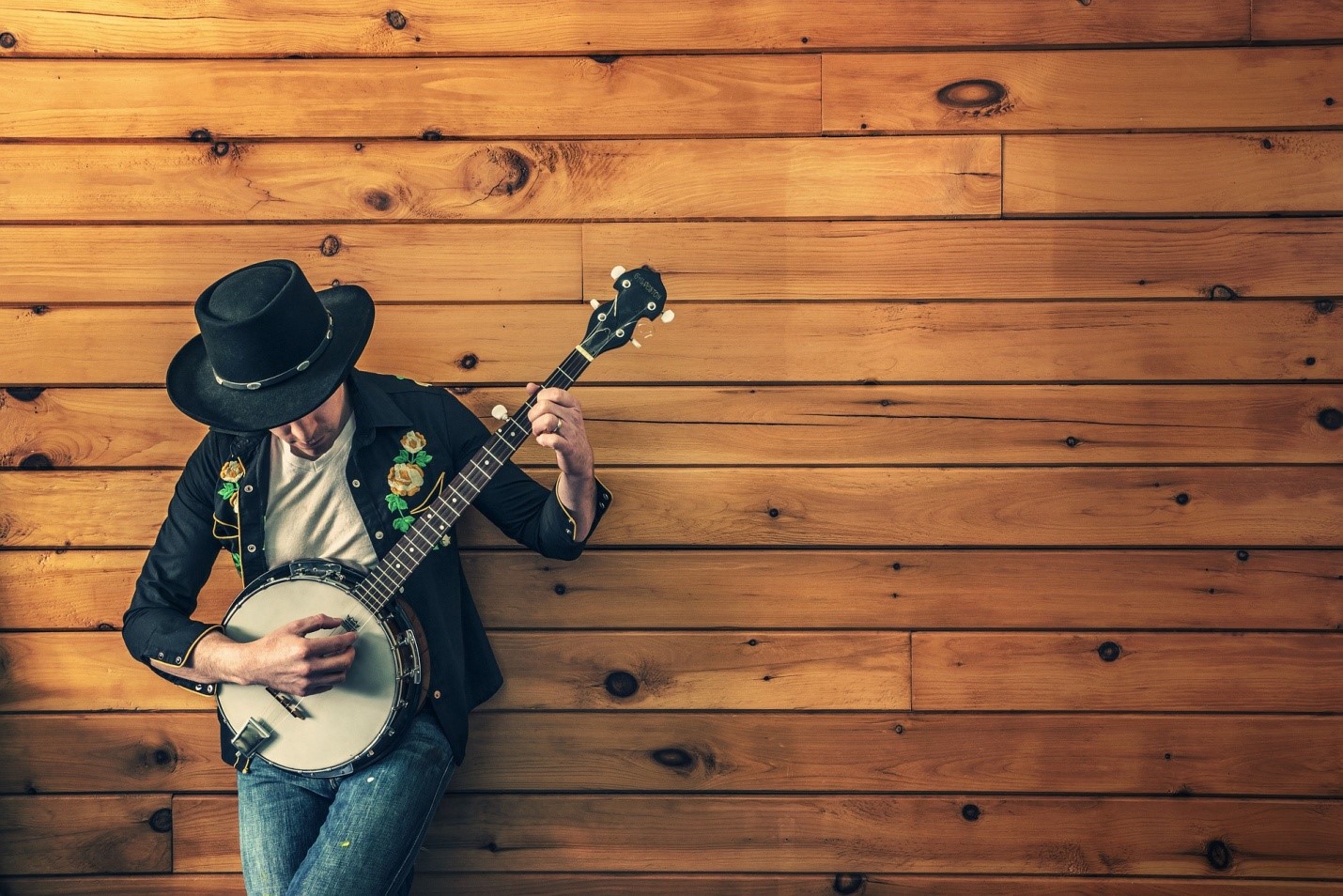 The Top Reasons Why More People Are Learning To Play The Banjo Today | My Zeo Person playing a banjo while leaning against a wooden wall