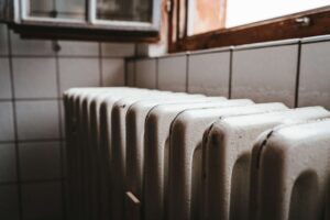 White cast-iron radiator along a tiled wall by an open window in a kitchen or utility room.